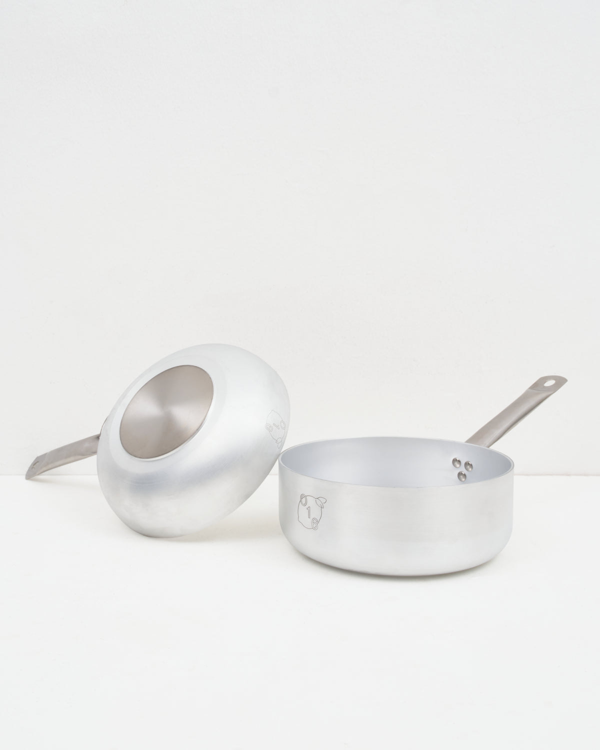 O16 lille aluminiumskokkesaet med vendt stegepande og kasserolle fra Osteria 16 — studiebillede der viser bund og form | O16 small aluminium cookware bundle with an upturned frying pan and saucepan by Osteria 16 — studio shot showing base and form