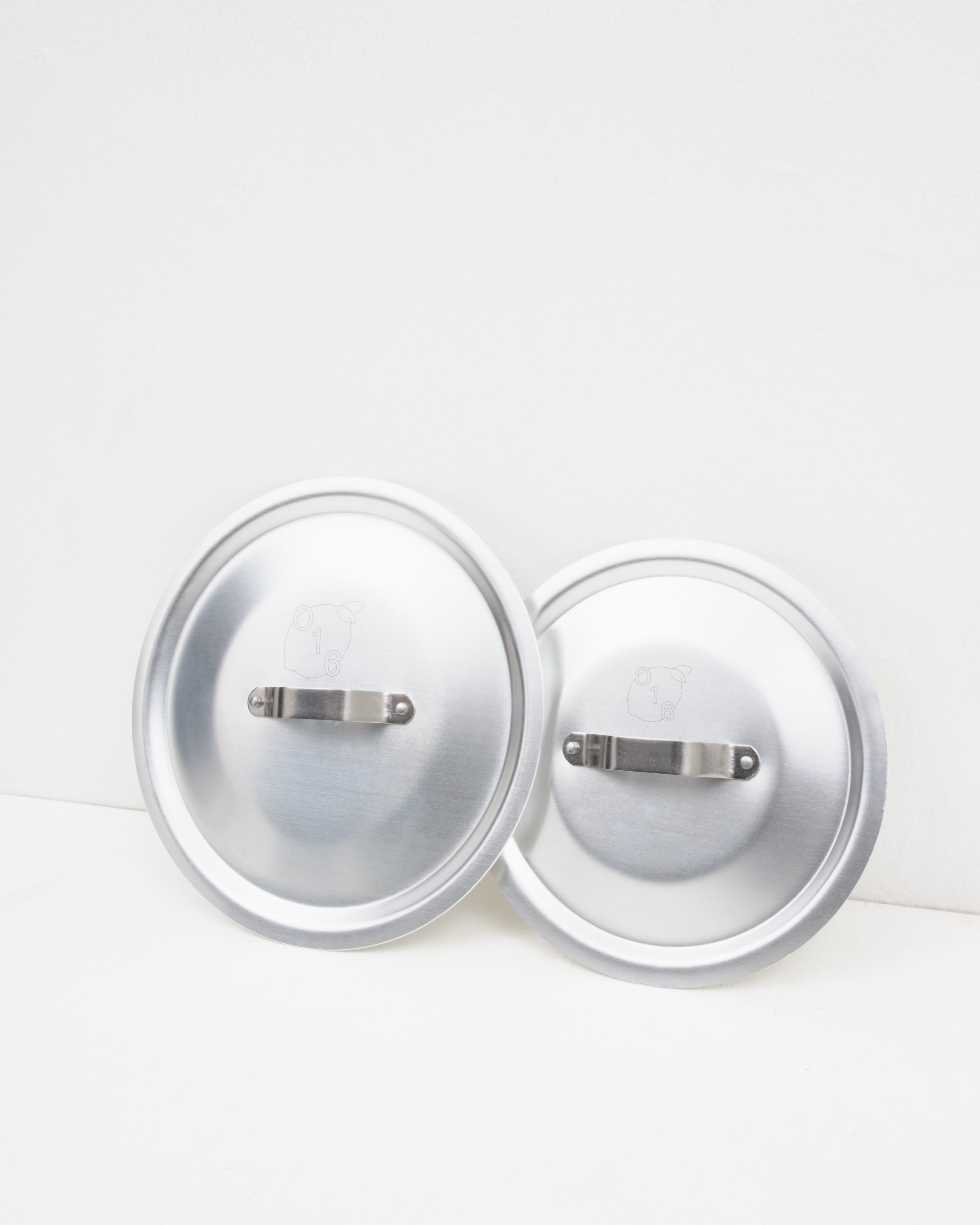 Studio: O16 to aluminiumslåg med stålgreb stillet side om side fra Osteria 16 — studieproduktbillede på hvid baggrund | O16 two aluminium lids with steel handles set side by side by Osteria 16 — studio product shot on white background