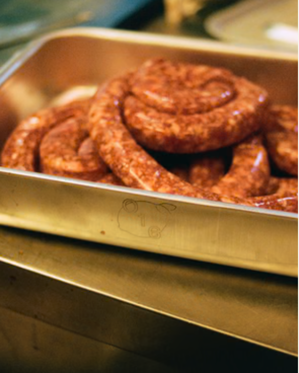 In-use: Snoede italienske pølser, salsiccia, i et O16 stålfad på restaurantkøkkenets bord hos Osteria 16. | Coiled Italian salsiccia sausages in an O16 stainless steel tray on the Osteria 16 restaurant kitchen counter.