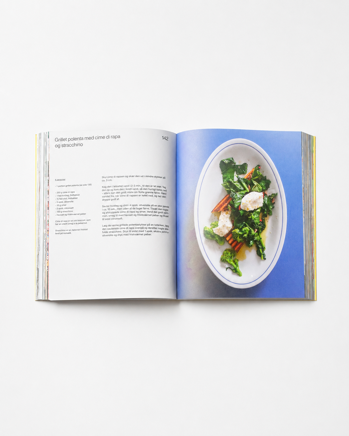 !Pages: Osteria 16 kogebog opslået på side 142 — grillet polenta med cime di rapa og stracchino på oval tallerken mod blå baggrund | Osteria 16 cookbook open at page 142 — grilled polenta with cime di rapa and stracchino on an oval plate against blue