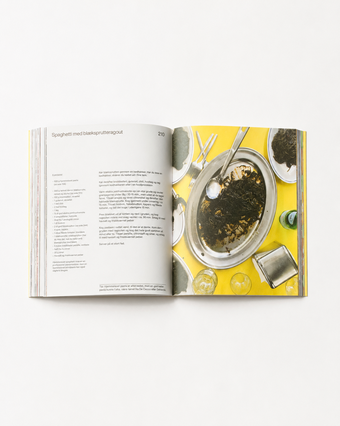 !Pages: O16 kogebog side 210 — spaghetti med blæksprutteragout på sølvfad mod gul bordflade, analogt madfoto | O16 cookbook page 210 — spaghetti with squid-ink ragu on a silver platter against a yellow table, analogue food photo