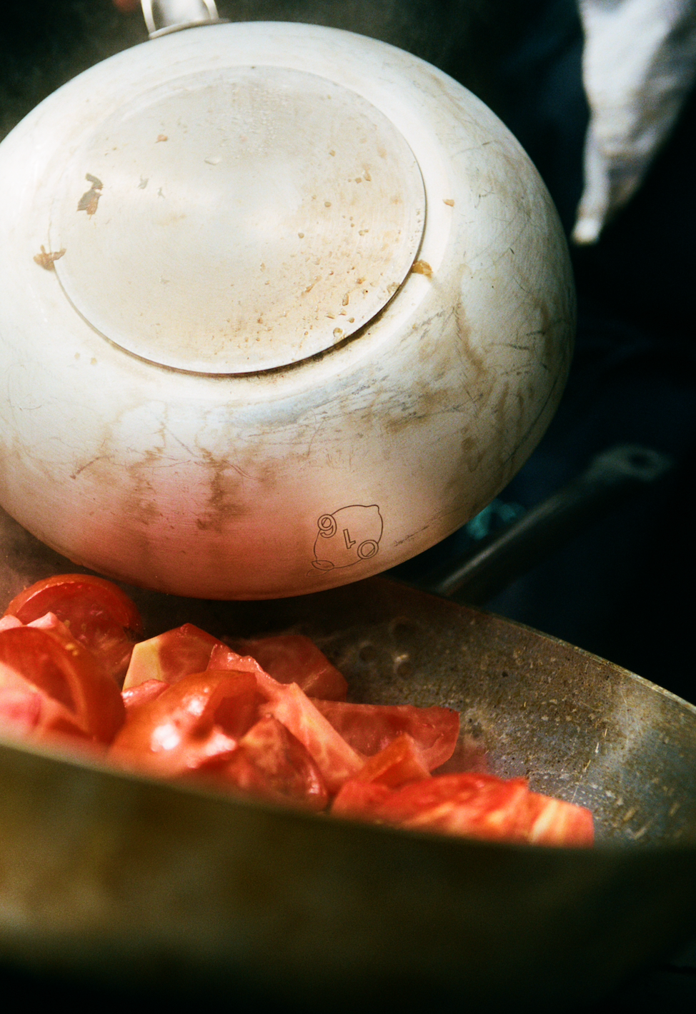 In use: Hvid emaljegryde med O16-citronlogo over en dampende pande med friske tomater, analog film, Osteria 16-køkken | White enamel pot with O16 lemon logo above a steaming pan of fresh tomatoes, analogue film, Osteria 16 kitchen