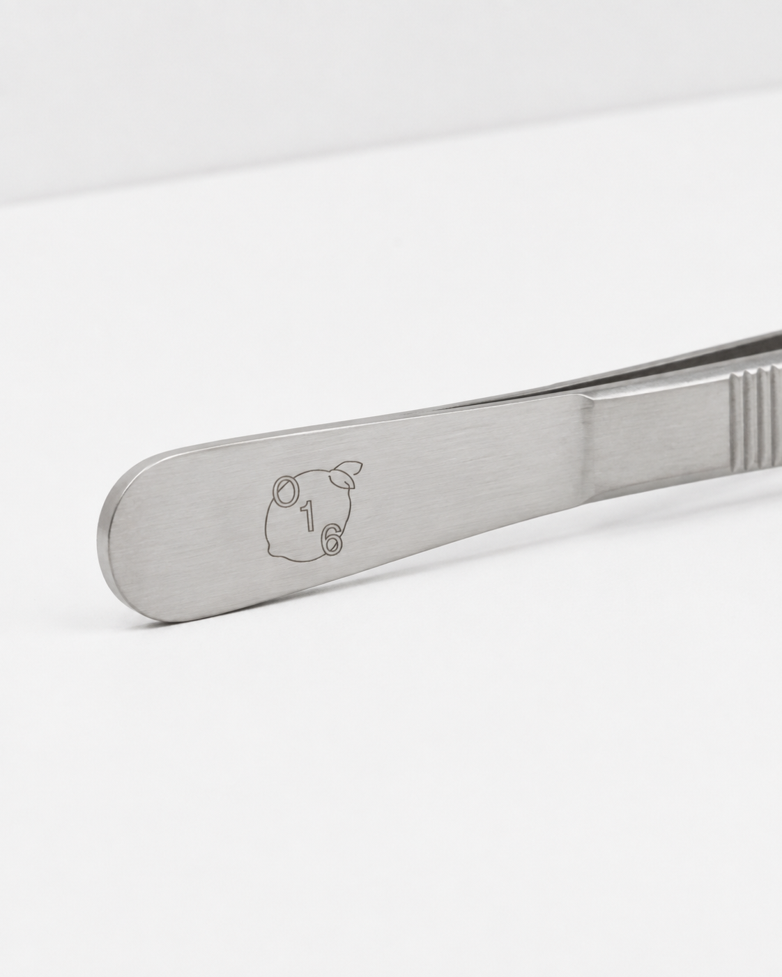 Studio: Nærbillede af det graverede O16-citronlogo på håndtaget af Pinze køkkentangen i rustfrit stål, studieshot | Close-up of the engraved O16 lemon logo on the handle of the stainless steel Pinze kitchen tongs, studio shot