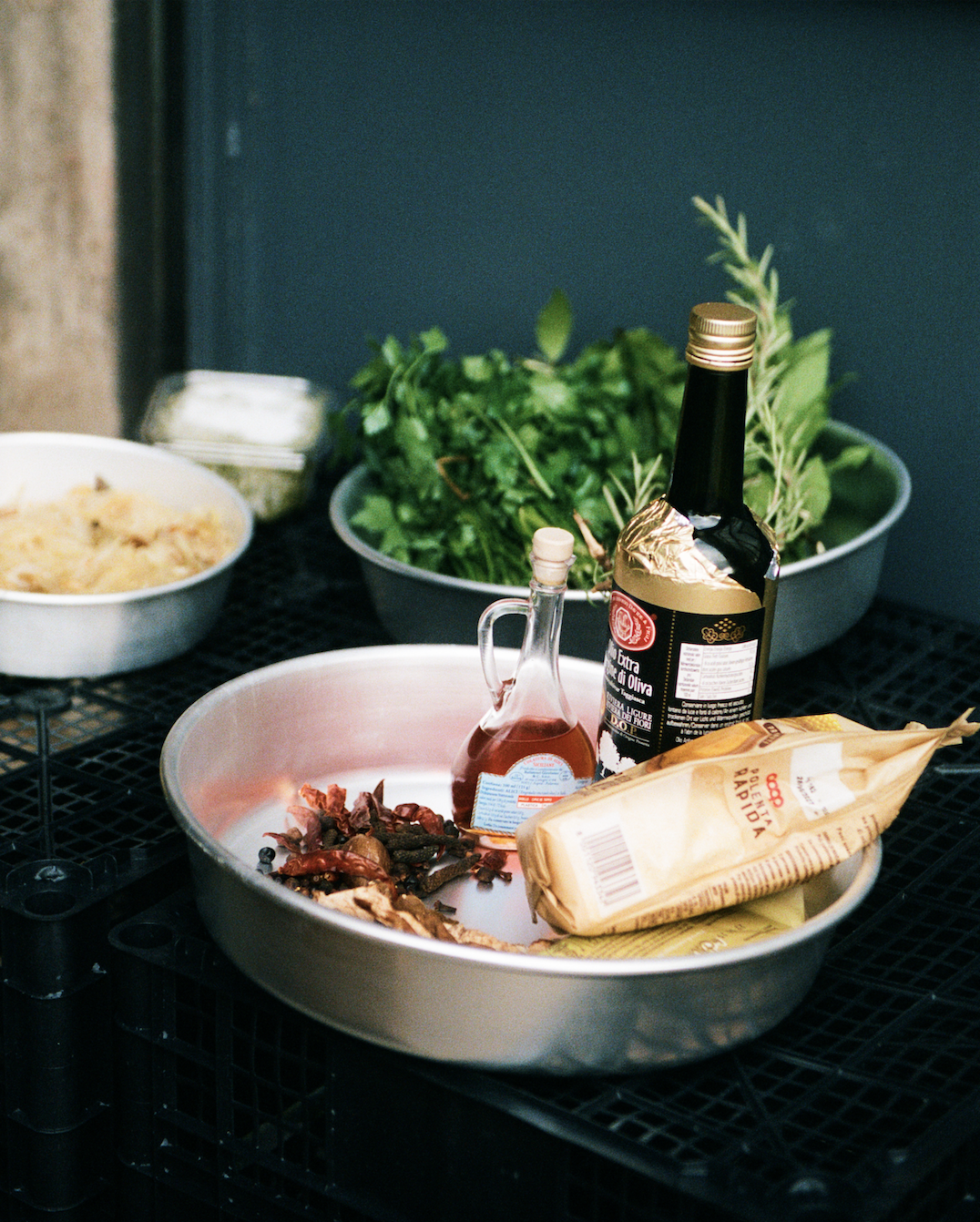 In-use: Osteria 16 mise en place — aluminiumsfade med friske urter, tørret chili, olivenolie og polenta på sorte kasser, analog film | Osteria 16 mise en place — aluminium dishes with fresh herbs, dried chilli, olive oil and polenta on black crates, analogue film
