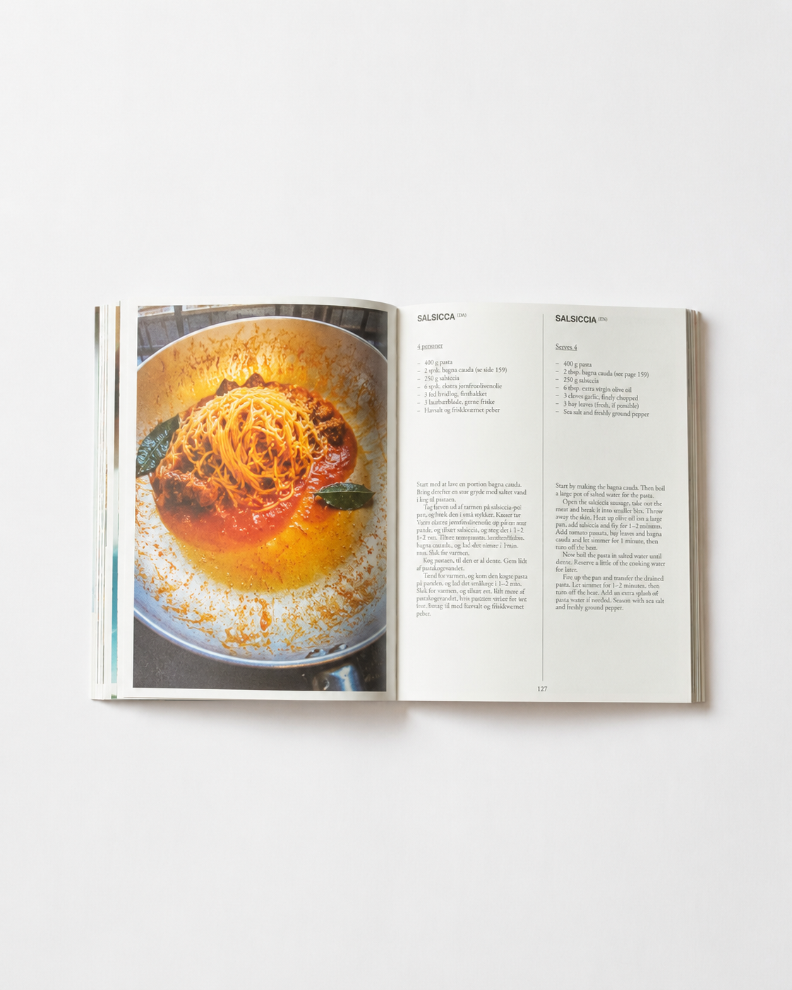 !Pages: Opslag i O16 kogebog med Salsiccia-opskriften og foto af spaghetti i tomat-pølsesauce i pande. | Spread in the O16 cookbook showing the Salsiccia recipe with a photo of spaghetti in tomato-sausage sauce in a pan.