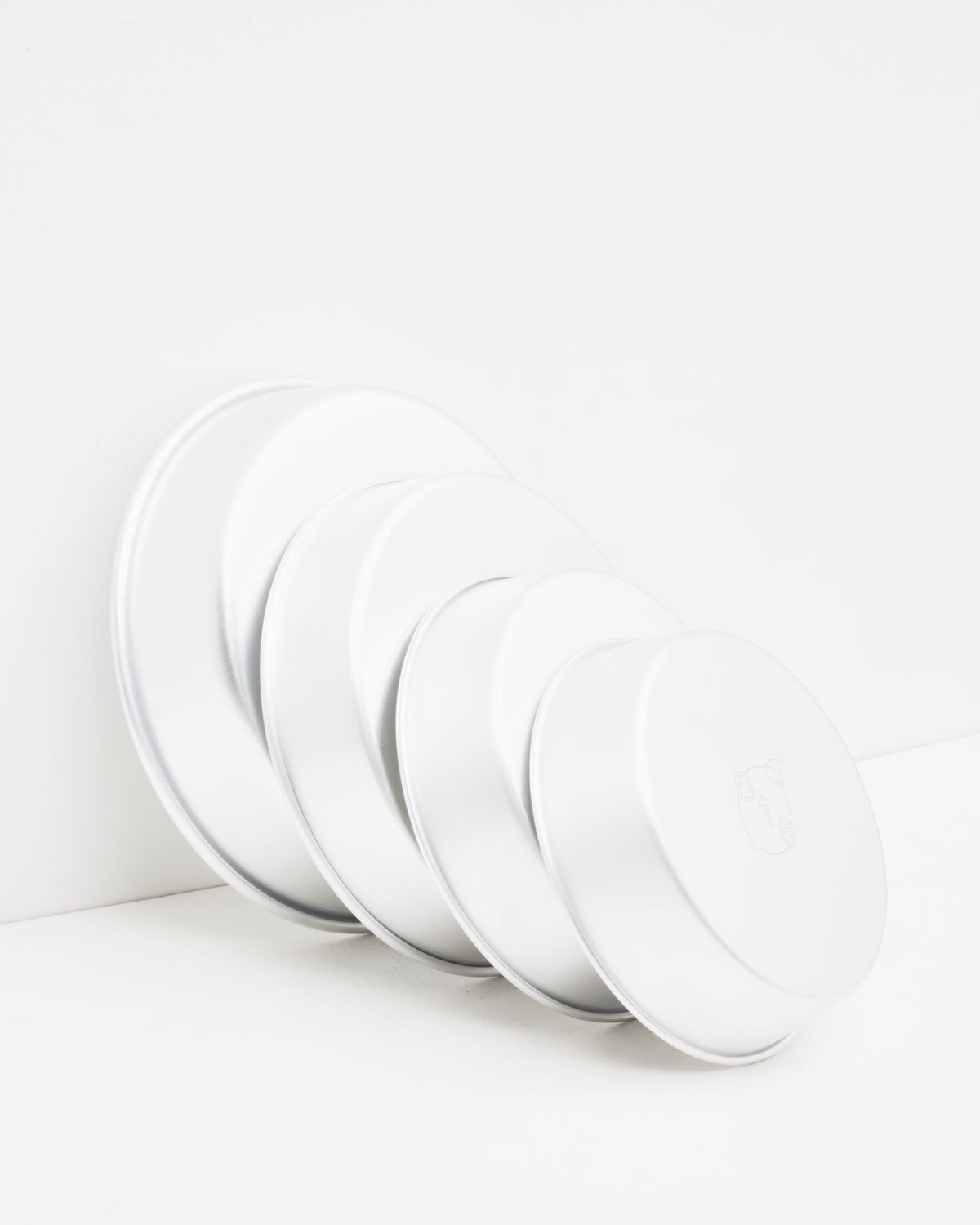 O16 dybe runde ovnfaste aluminiumsfade i flere størrelser stablet mod væg — detaljebillede af graderede størrelser, Osteria 16 | O16 deep round ovenproof aluminium dishes in several sizes stacked against a wall — size-graduated detail shot, Osteria 16