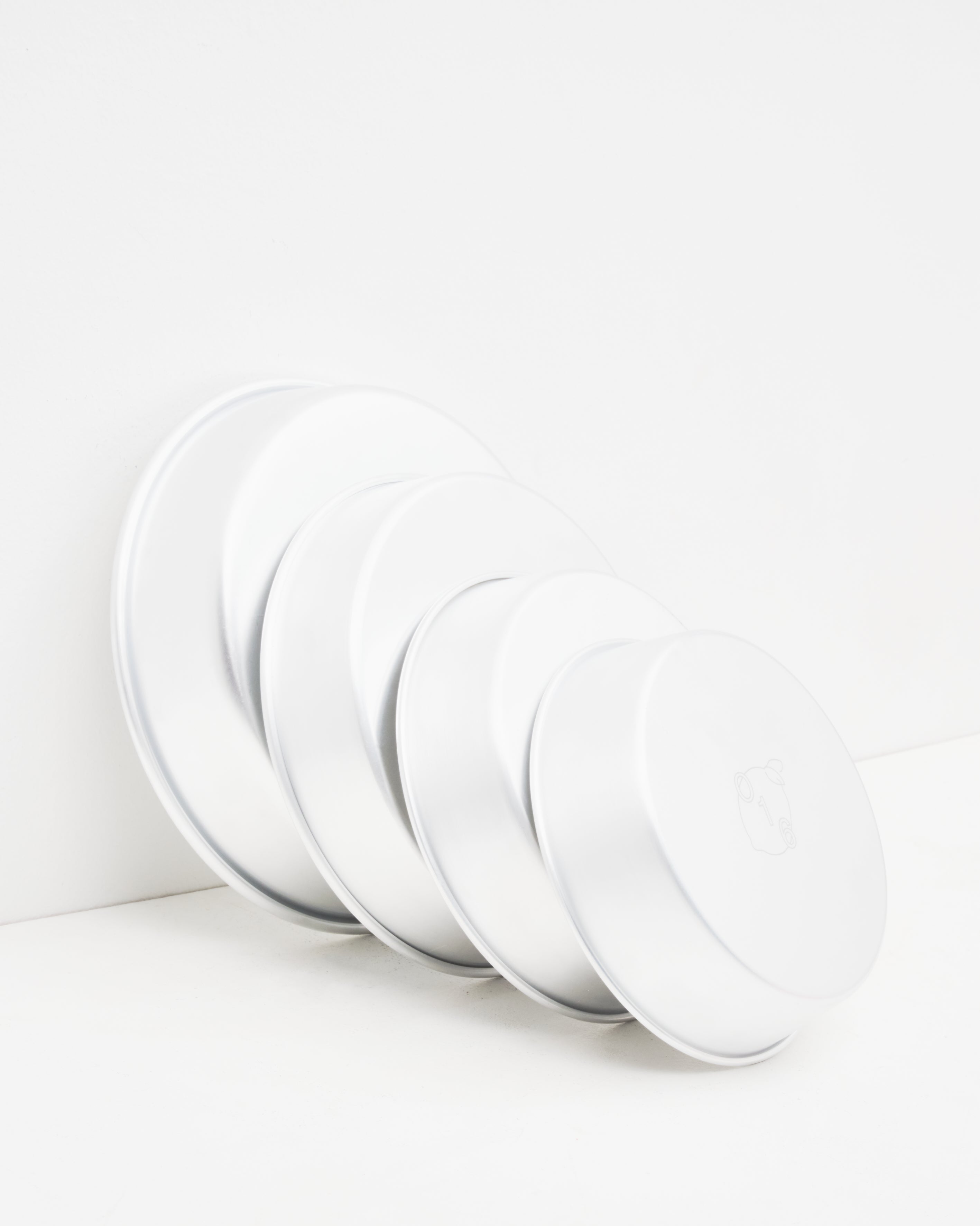 O16 dybe runde ovnfaste aluminiumsfade i flere størrelser stablet mod væg — detaljebillede af graderede størrelser, Osteria 16 | O16 deep round ovenproof aluminium dishes in several sizes stacked against a wall — size-graduated detail shot, Osteria 16