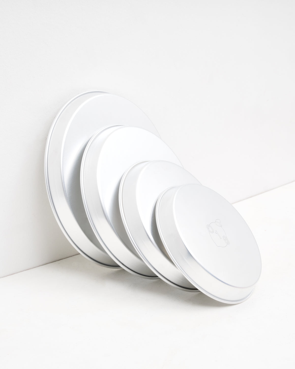 O16 runde aluminiumsbageforme i flere størrelser stablet mod væg — detalje af graderede størrelser med logo, Osteria 16 | O16 round aluminium baking dishes in several sizes stacked against a wall — detail of graduated sizes with logo, Osteria 16