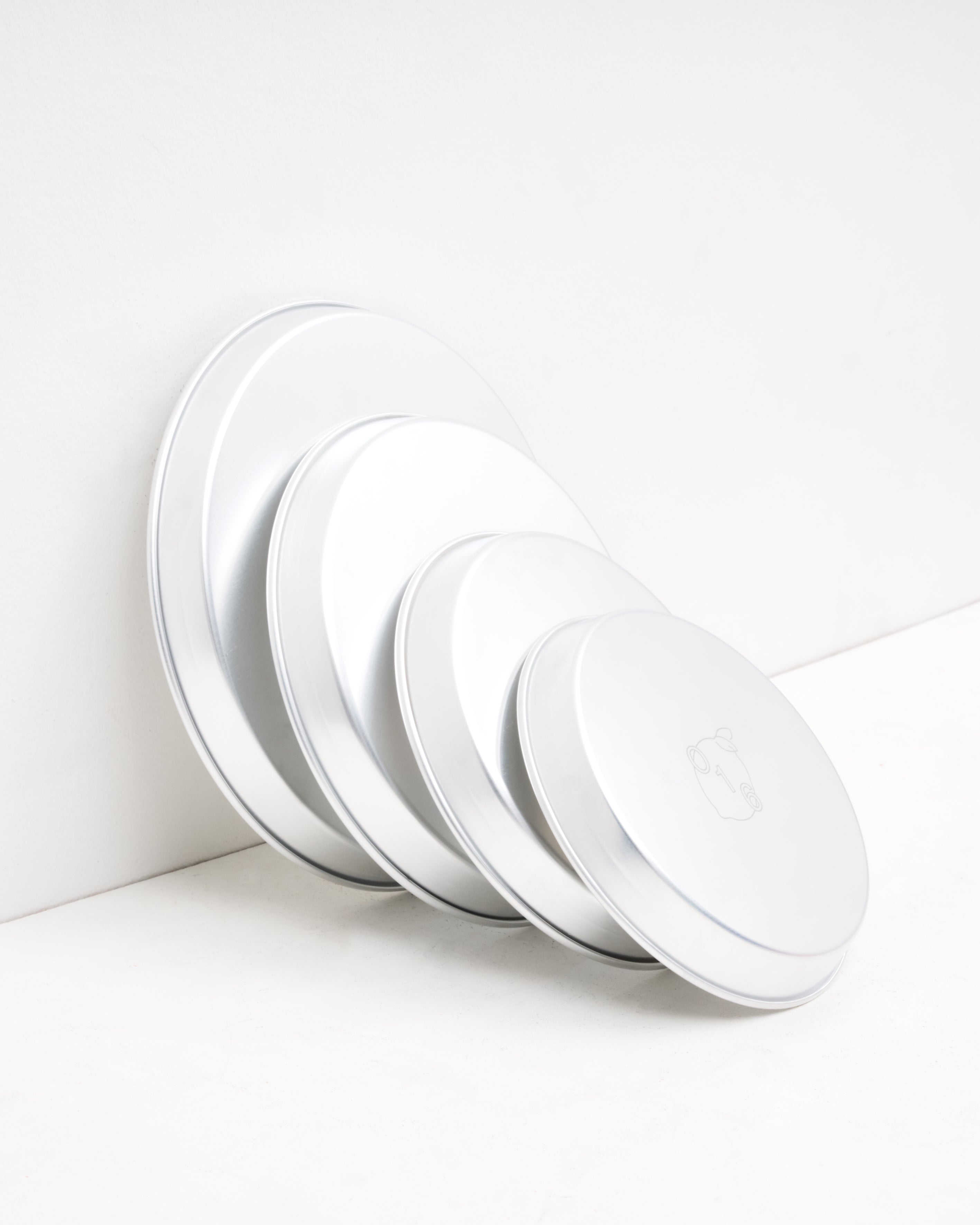 Studio: O16 runde aluminiumsbageforme i flere størrelser stablet mod væg — detalje af graderede størrelser med logo, Osteria 16 | O16 round aluminium baking dishes in several sizes stacked against a wall — detail of graduated sizes with logo, Osteria 16