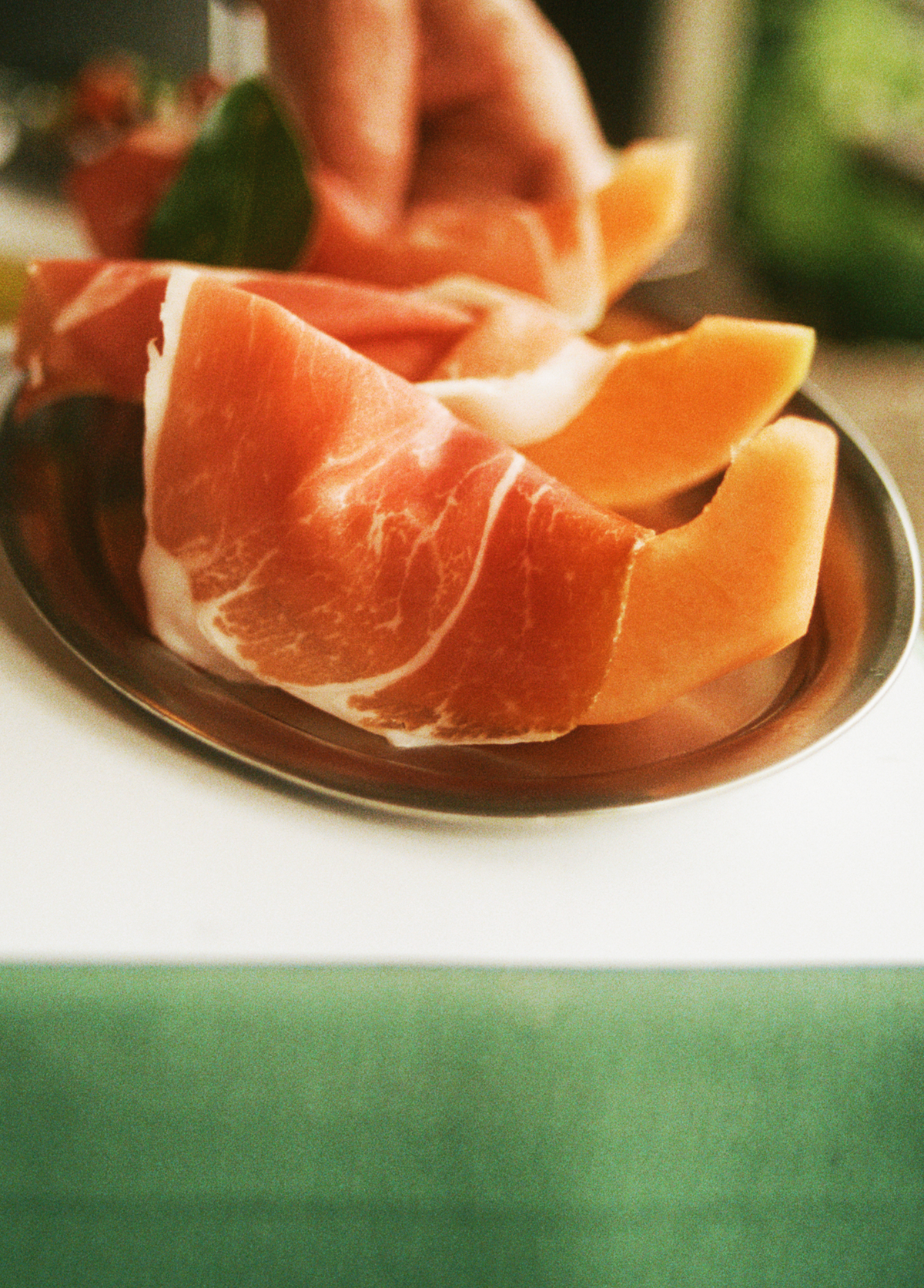 O16 Vassoio ovalt fad i stål med prosciutto og melon — italiensk forret i lifestyle-opstilling | O16 Vassoio oval stainless steel plate with prosciutto and melon — Italian antipasto in a lifestyle setting
