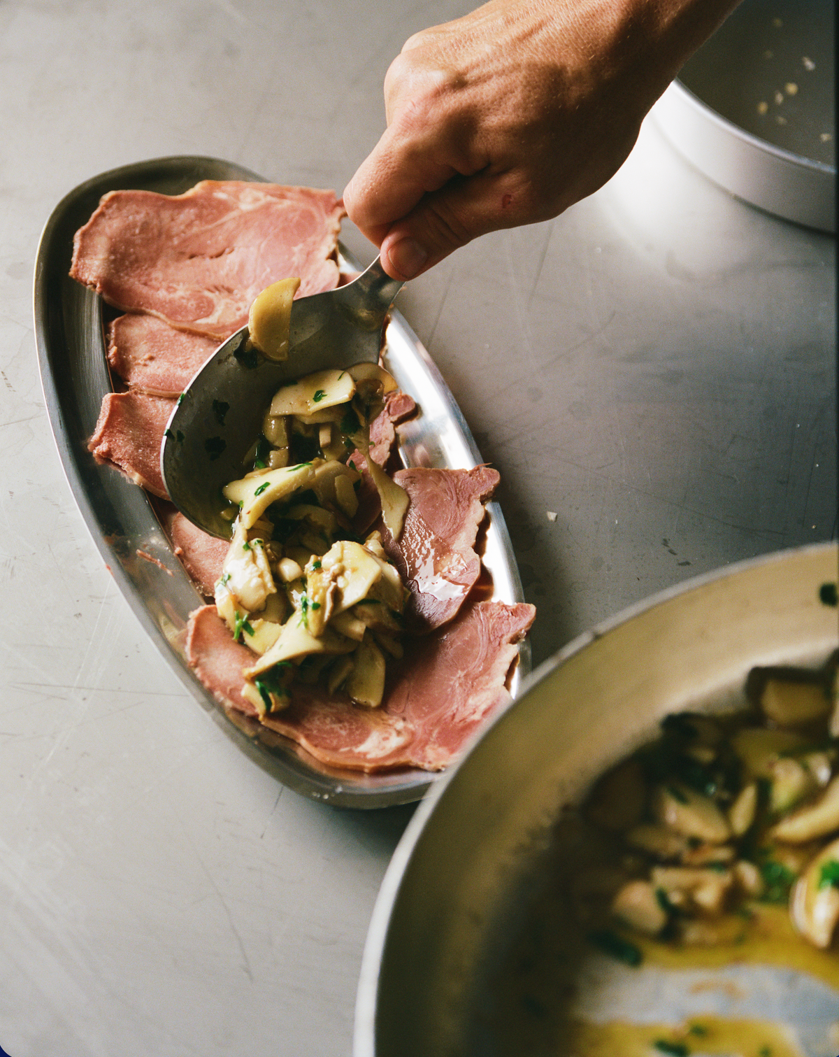 O16 Vassoio 2 ovalt stålfad med koldskåret kød og svampesalat — hånd anretter, lifestyle | O16 Vassoio 2 oval steel platter with cold cuts and mushroom salad, hand plating — lifestyle shot