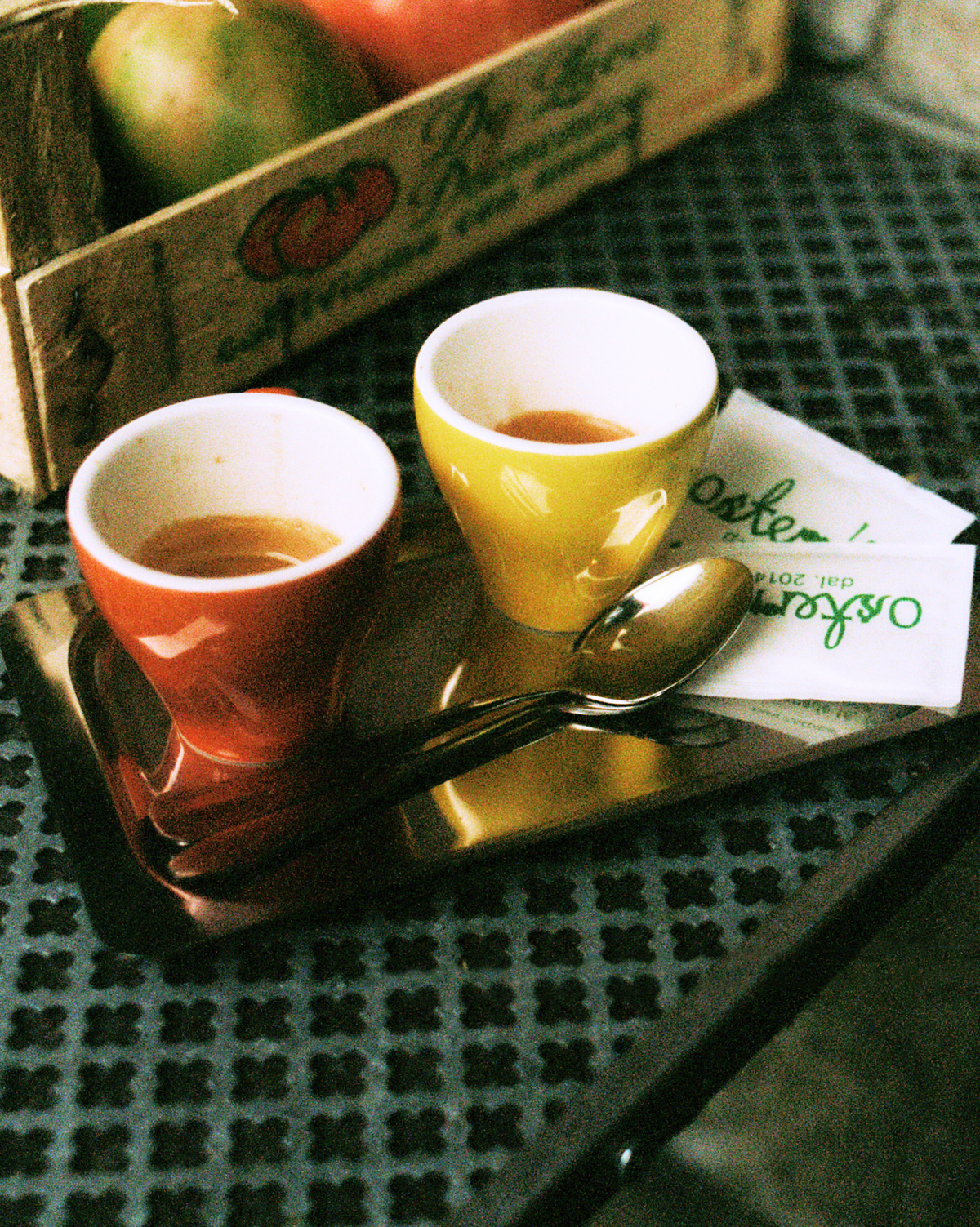 O16 Vassoio 3 kvadratisk stålfad med to espressokopper og ske ved en tomatkasse og Osteria 16-servietter — lifestyle | O16 Vassoio 3 square steel tray with two espresso cups and a spoon beside a tomato crate and Osteria 16 napkins — lifestyle shot