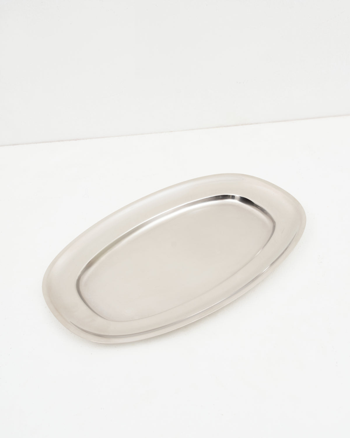 O16 Vassoio 5 stort ovalt serveringsfad i rustfrit stål fra Osteria 16 — vinklet lifestyle-studiebillede på hvid | O16 Vassoio 5 large oval stainless steel serving platter by Osteria 16 — angled lifestyle studio shot on white