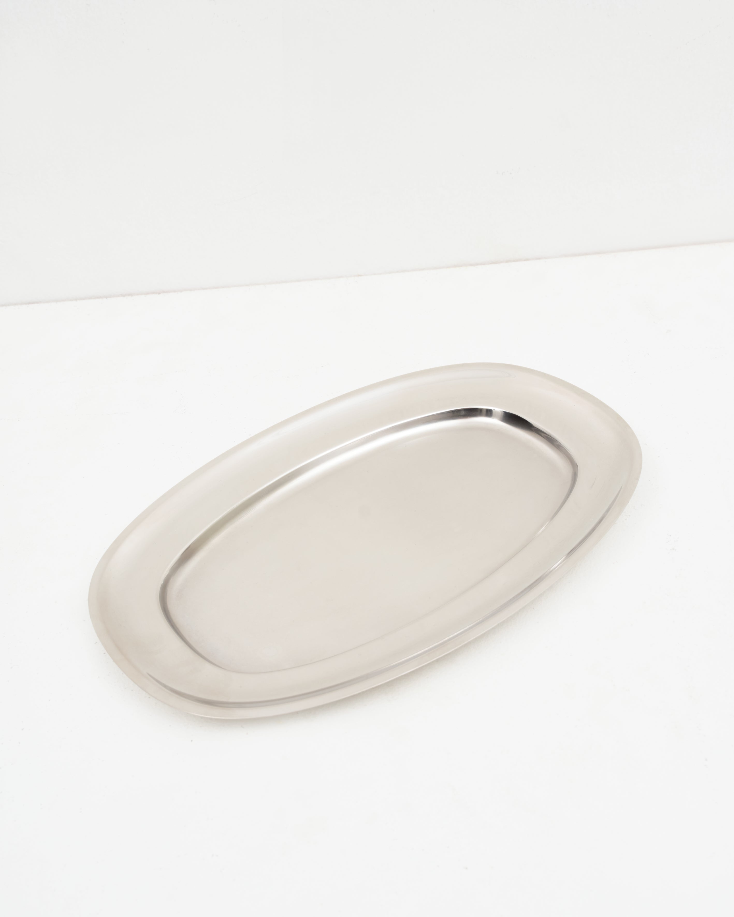 Studio: O16 Vassoio 5 stort ovalt serveringsfad i rustfrit stål fra Osteria 16 — vinklet lifestyle-studiebillede på hvid | O16 Vassoio 5 large oval stainless steel serving platter by Osteria 16 — angled lifestyle studio shot on white