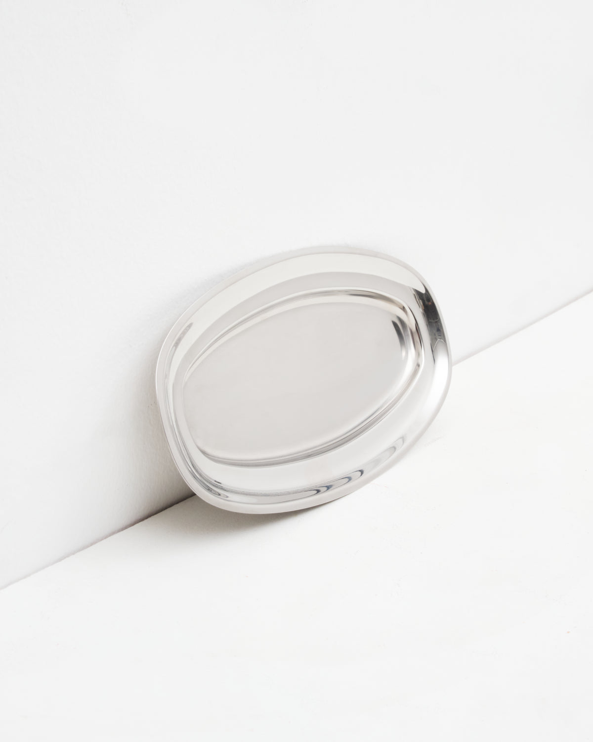 O16 Osteria 16 Vassoio 2 mellemstort ovalt serveringsfad i børstet rustfrit stål lænet mod væg, nærbillede af overfladen | O16 Osteria 16 Vassoio 2 medium oval stainless steel serving tray leaning against a wall, close-up of the surface
