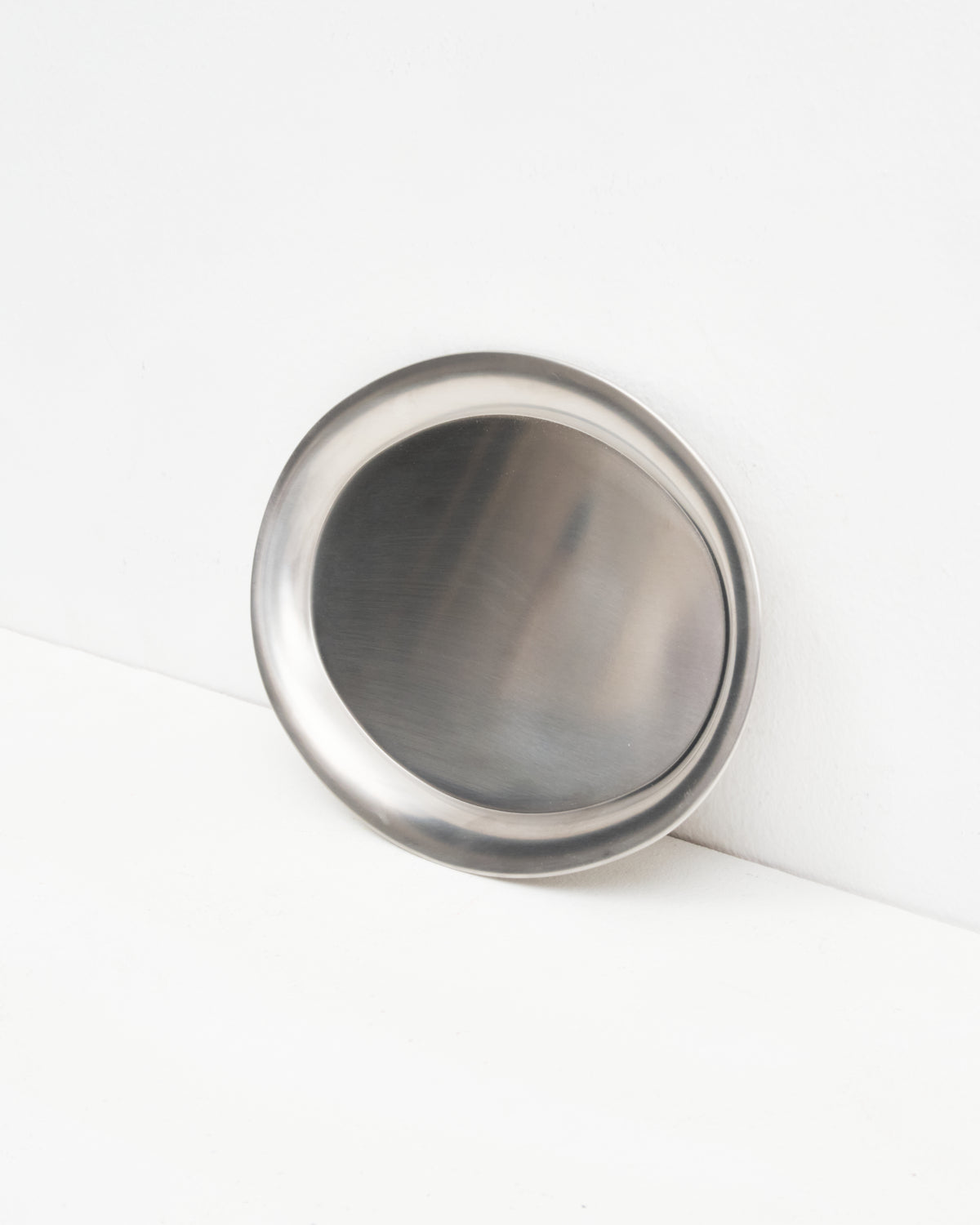 O16 Osteria 16 Vassoio lille serveringsfad i børstet rustfrit stål lænet mod væg, nærbillede af den skålformede overflade | O16 Osteria 16 Vassoio small stainless steel serving tray leaning against a wall, close-up of the concave brushed surface