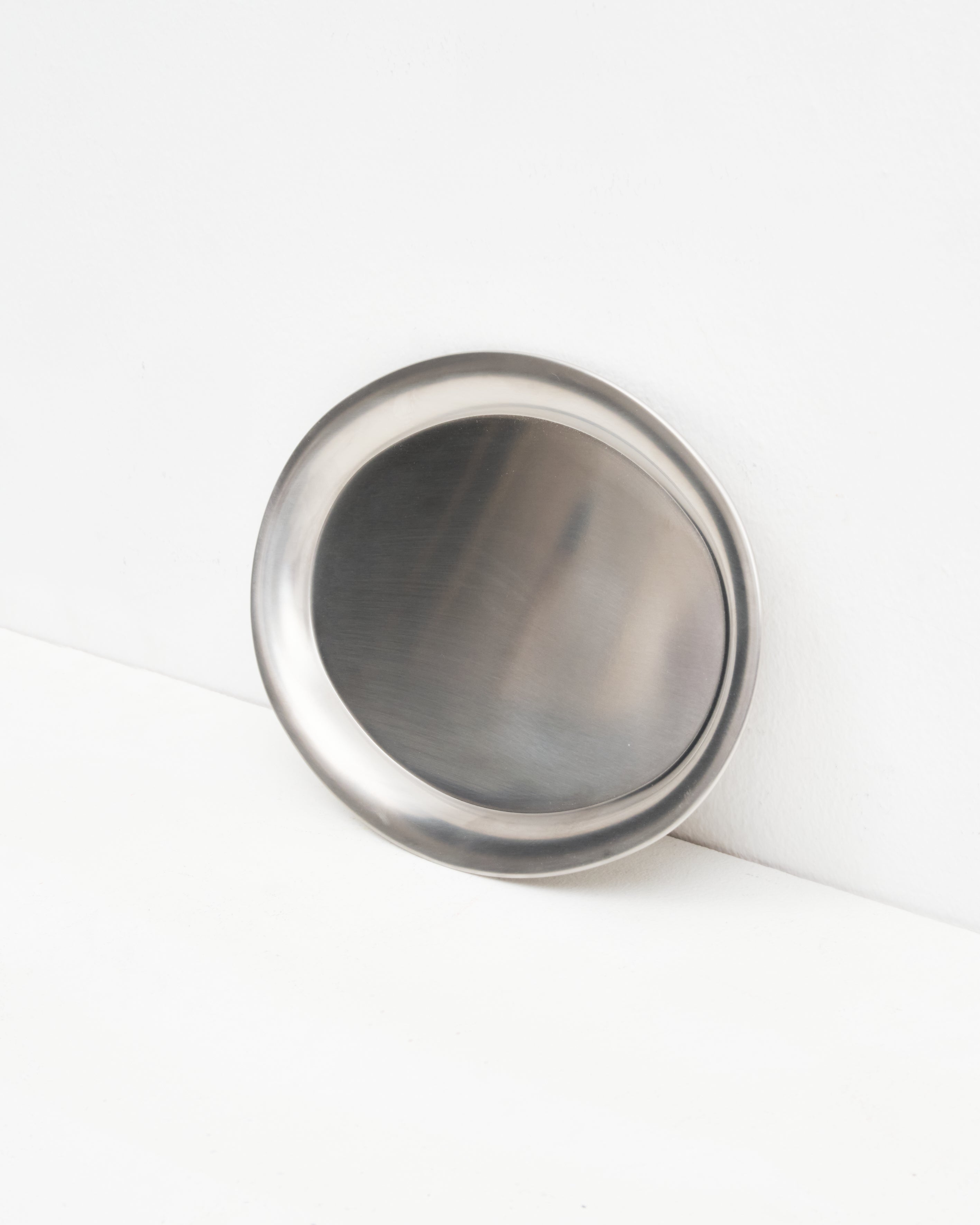 Studio: O16 Osteria 16 Vassoio lille serveringsfad i børstet rustfrit stål lænet mod væg, nærbillede af den skålformede overflade | O16 Osteria 16 Vassoio small stainless steel serving tray leaning against a wall, close-up of the concave brushed surface