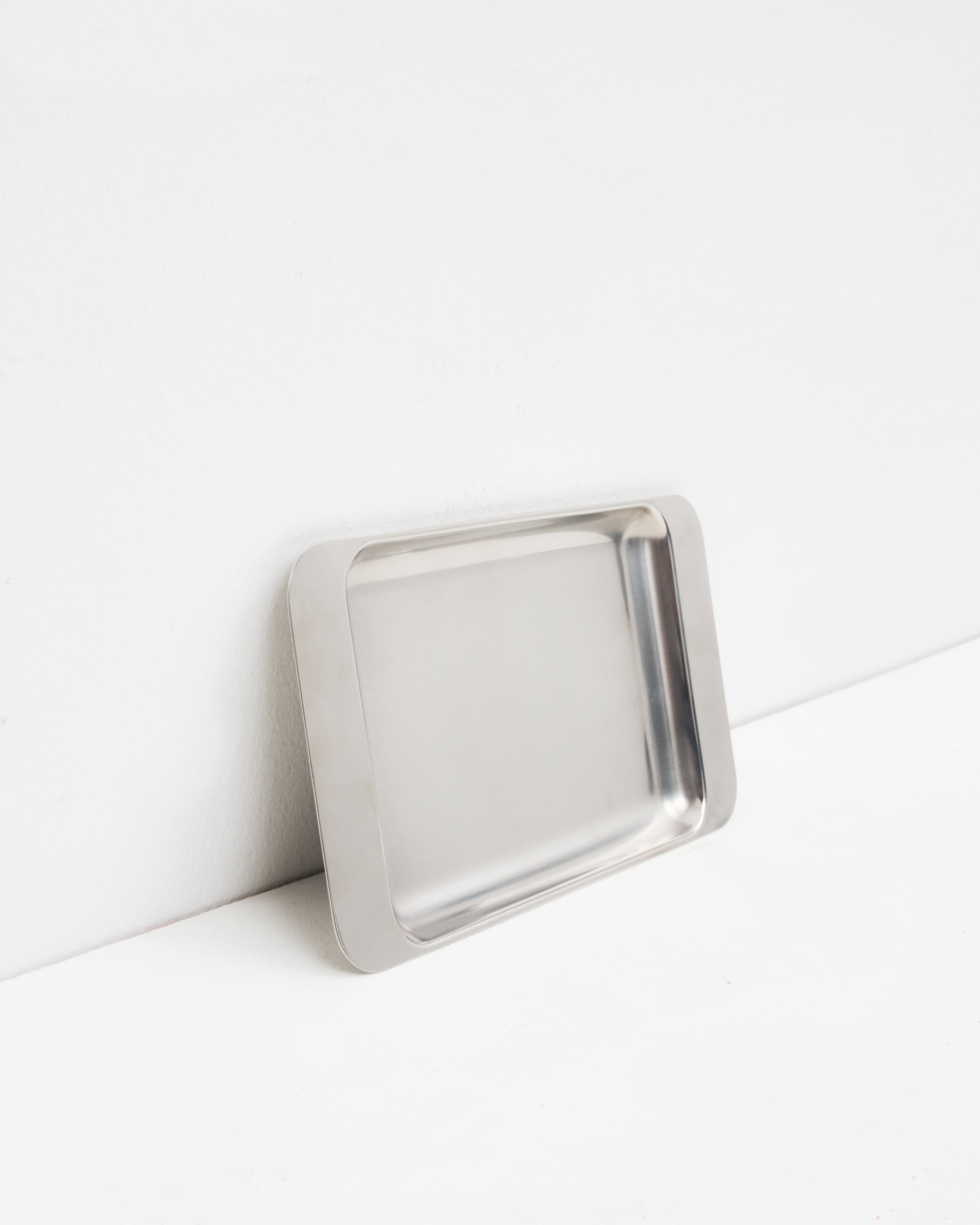 O16 Osteria 16 Vassoio 4 stort rektangulært serveringsfad i børstet rustfrit stål lænet mod væg, nærbillede af overfladen | O16 Osteria 16 Vassoio 4 large rectangular stainless steel serving tray leaning against a wall, close-up of the surface
