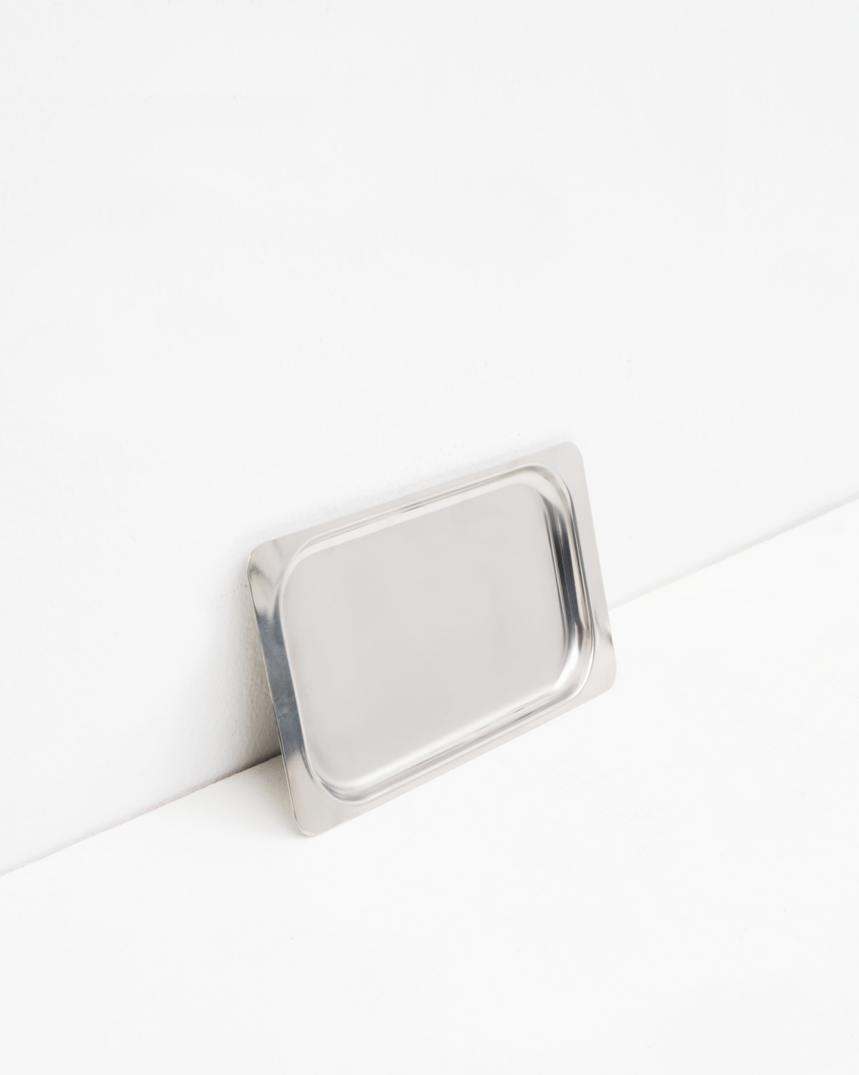 O16 Osteria 16 Vassoio 3 lille rektangulært serveringsfad i børstet rustfrit stål lænet mod væg, nærbillede af overfladen | O16 Osteria 16 Vassoio 3 small rectangular stainless steel serving tray leaning against a wall, close-up of the surface
