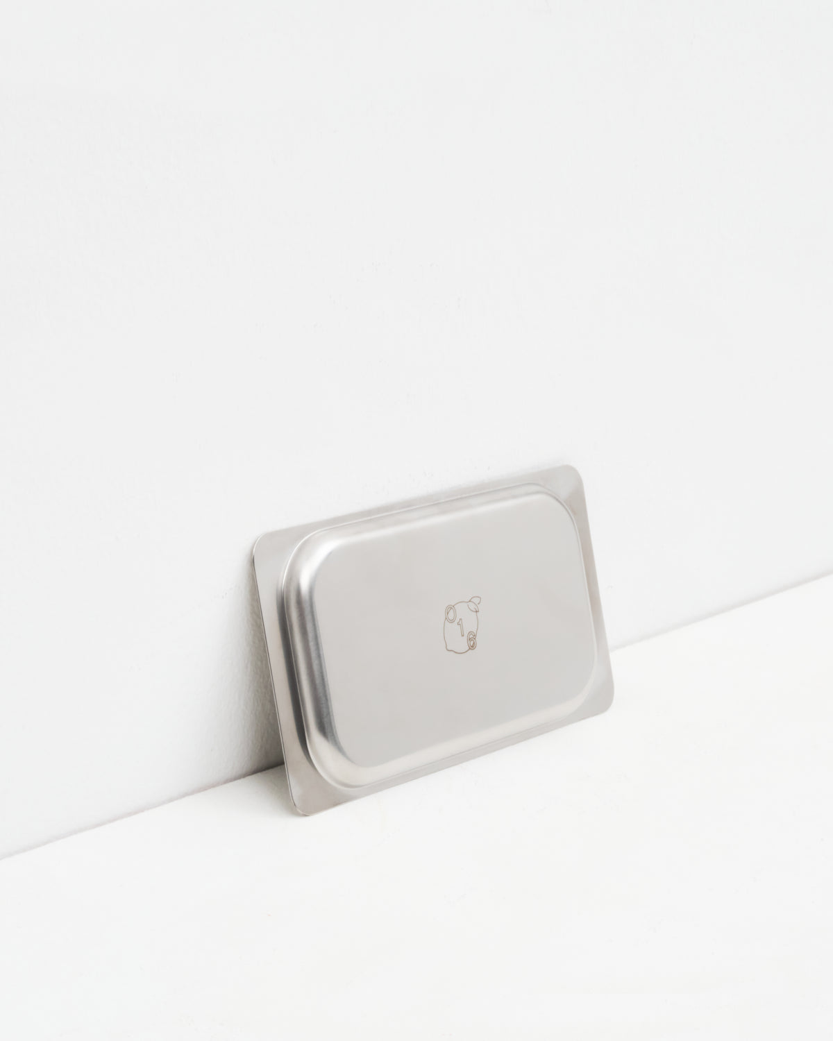 O16 Osteria 16 Vassoio 3 lille rektangulært serveringsfad i rustfrit stål lænet mod væg med indgraveret O16-logo, detaljebillede | O16 Osteria 16 Vassoio 3 small rectangular stainless steel serving tray leaning against a wall with engraved O16 logo, detail shot