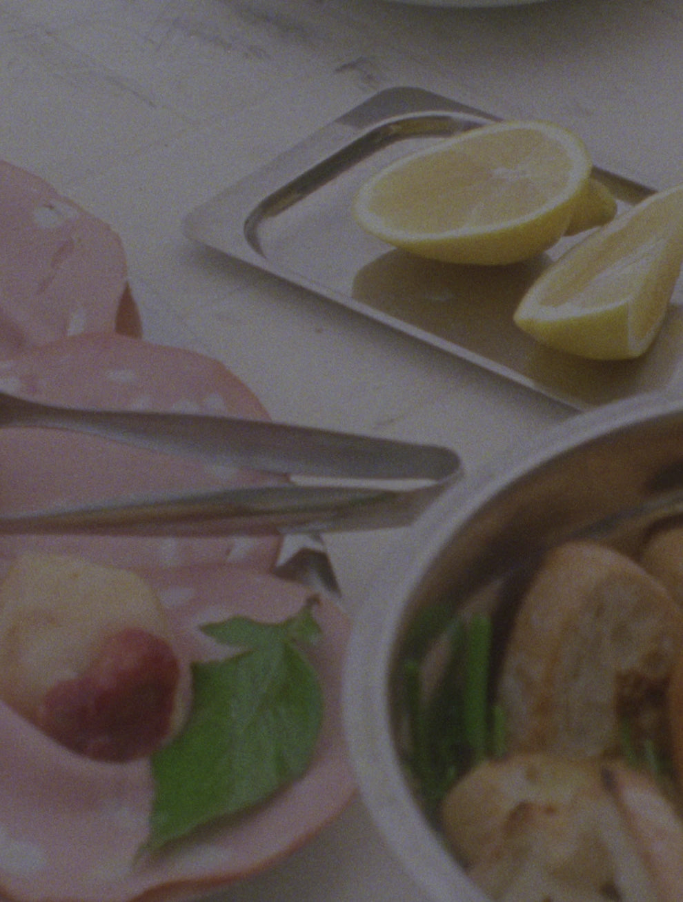 Motion: Editorielt videoklip fra O16 Osteria 16 — mortadella med basilikum, ståltang og citronhalve på et serveringsfad, analog film | Motion: Editorial O16 Osteria 16 motion clip — mortadella with basil, steel tongs and lemon halves on a serving tray, analogue film